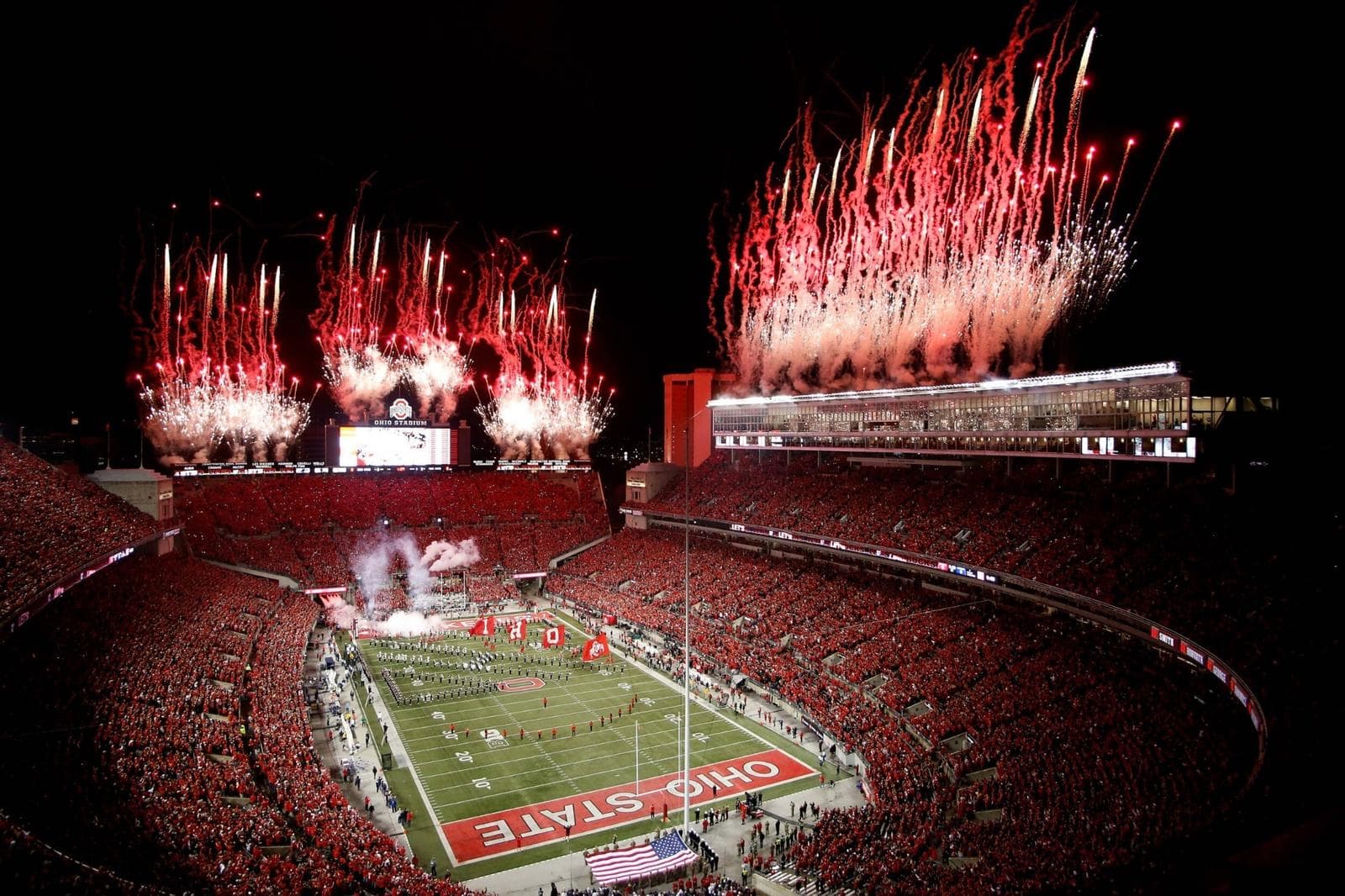 Ohio Stadium, the Horseshoe, during a night game — fireworks over a scarlet-packed crowd as the Ohio State band takes the field